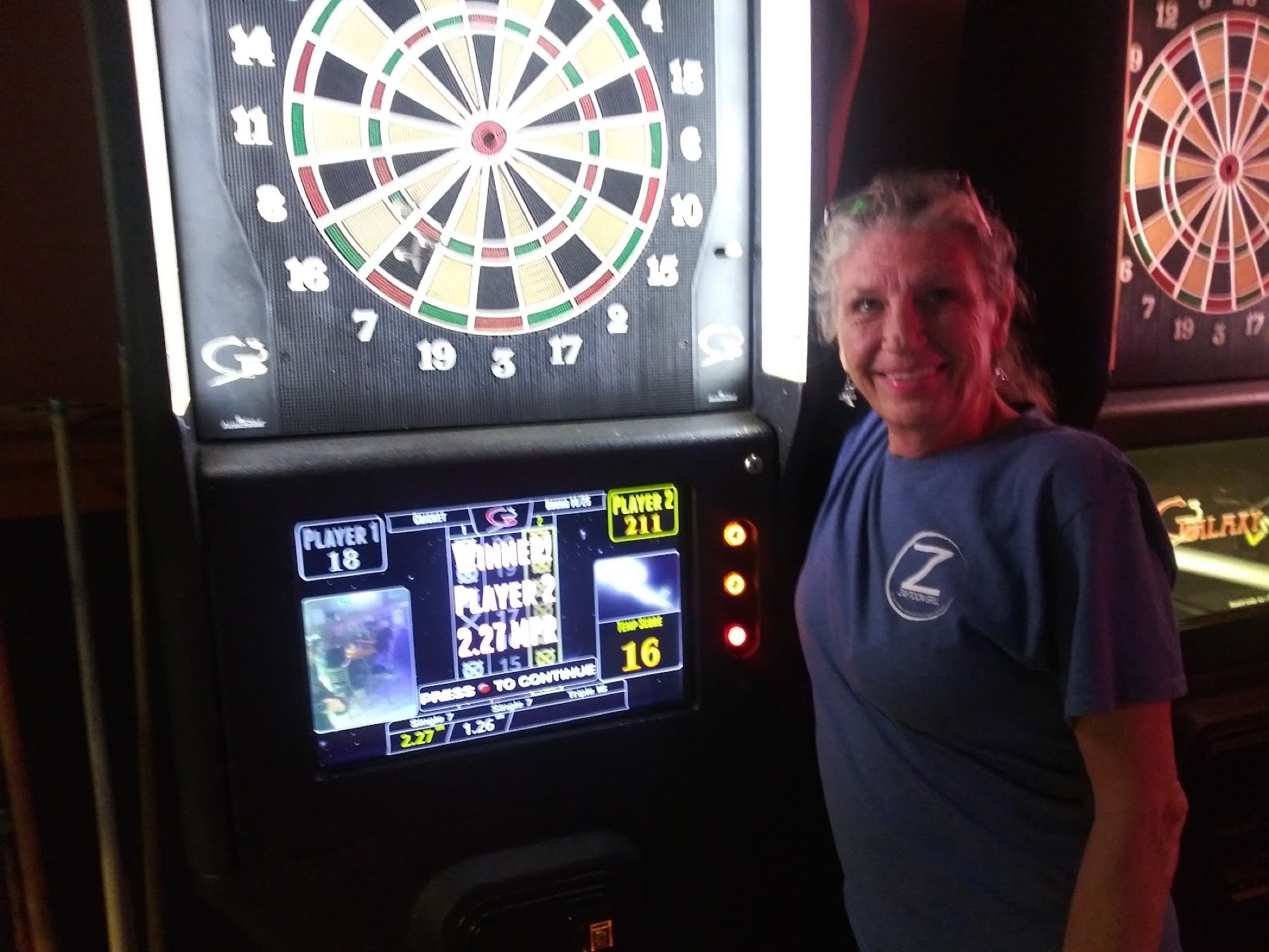 A lit electronic dart board with a player smiling beside it