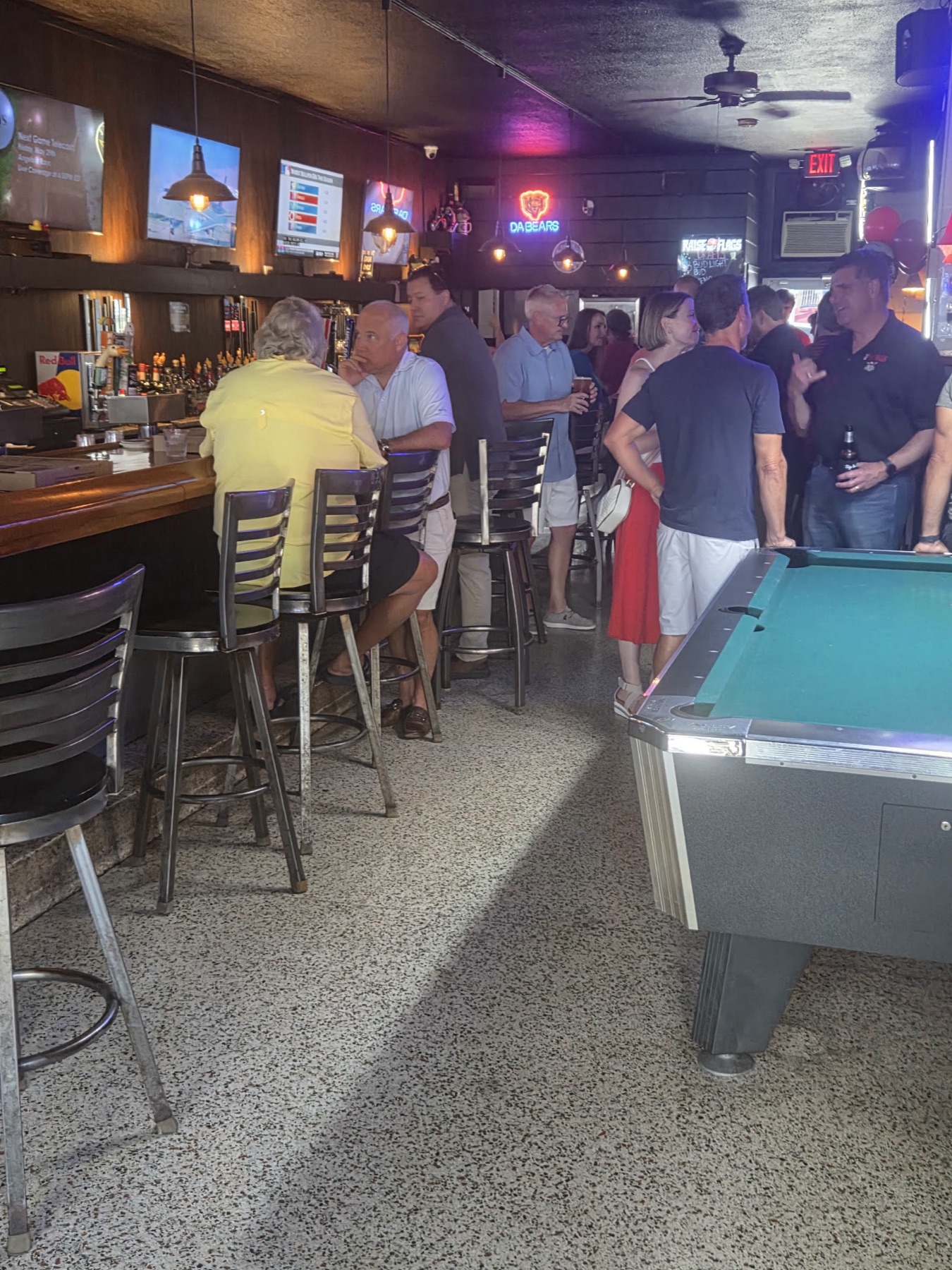 People at the bar next to the green-felt pool table under warm lights