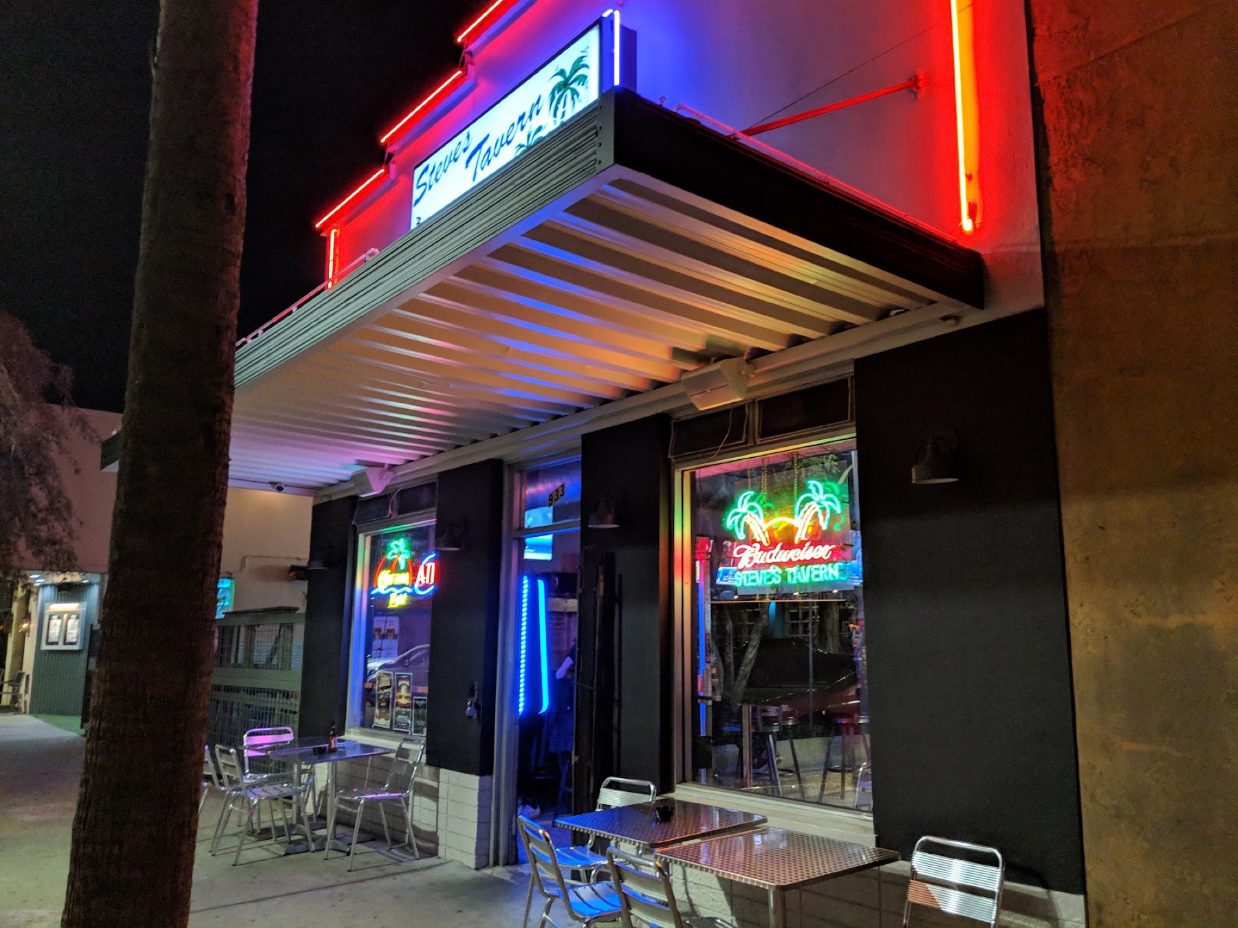 Steve’s Tavern neon sign and awning glowing over sidewalk tables at night